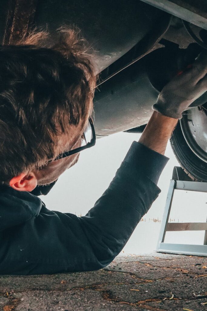 Mechanic skillfully repairing car undercarriage in outdoor setting with tools.